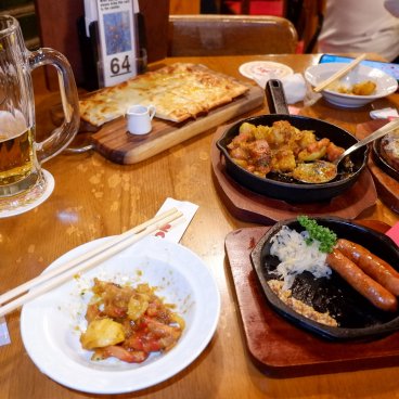 Ginza Lion 7-chome (Tokyo), sélection de plats (saucisses, curry de pommes de terre, flammekueche) avec de la bière Sapporo