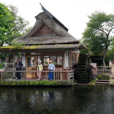 Oshino Hakkai (Fujiyoshida), Visiteurs contemplant l'eau limpide d'un étang près d'une maisonnette à toit de chaume